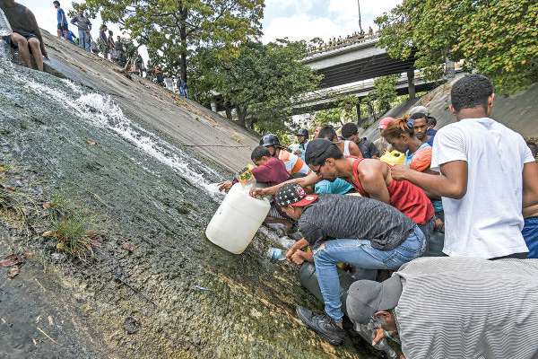 DESESPERACIÓN. Ante la escasez, decenas de personas buscan agua en el río Guaire, en Caracas. Foto: AFP