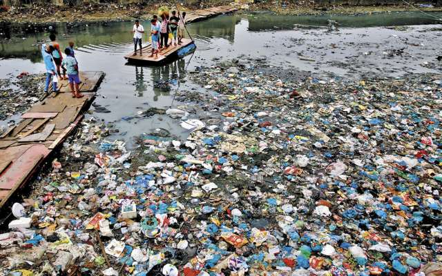 Un hombre guía una balsa a través de un
canal contaminado lleno de bolsas de plástico.FOTO: AP