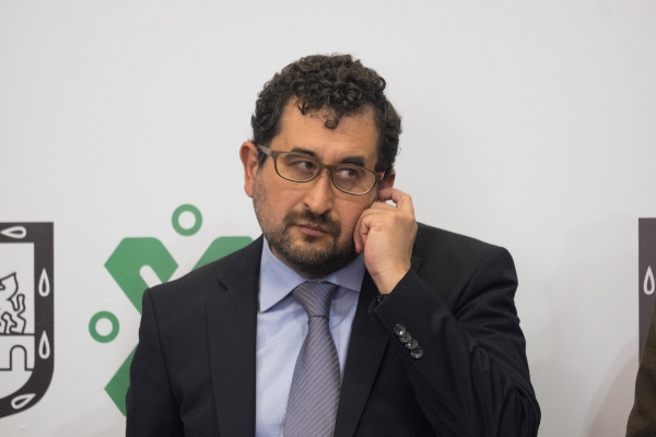 César Cravioto en mesa con pancarta de fondo con logo del gobierno de la Ciudad de México