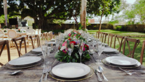 Mesa y sillas adornadas, con platos y cubierto, mantel y un arreglo de flores